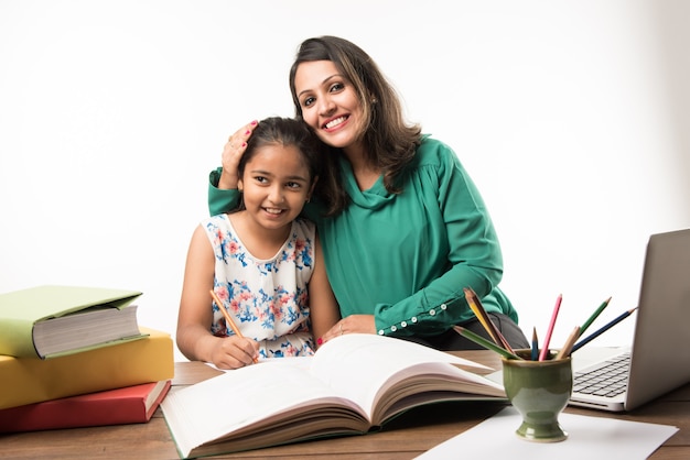 Indisches Mädchen, das mit Mutter oder Lehrer am Arbeitstisch mit Laptop-Computer, Büchern studiert und Spaß beim Lernen hat