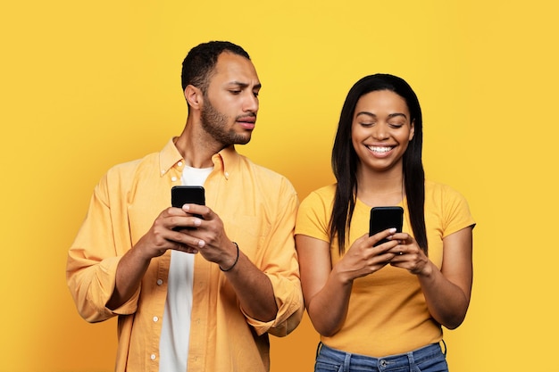 Indivíduo afro-americano milenar interessado olhando para o smartphone da esposa sorridente