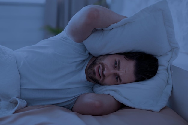 Individuo en cama que cubre su cabeza con la almohada