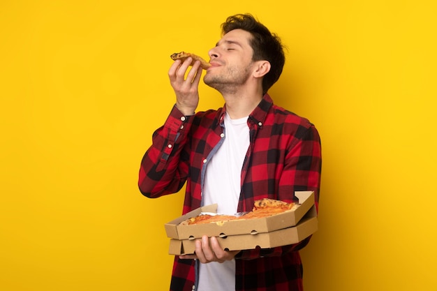 Individuo feliz que sostiene la caja que muerde la pizza en el estudio