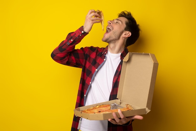 Individuo feliz que sostiene la caja que muerde la pizza en el estudio