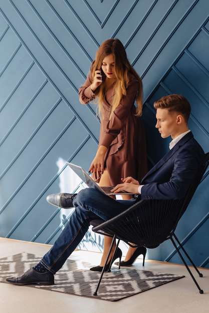 Individuo joven elegante con el ordenador portátil y la muchacha con el teléfono junto, hombre de negocios joven