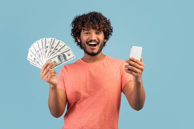 Individuo oriental feliz que sostiene el teléfono celular y el dinero en efectivo