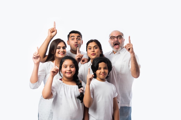 Indn familia multigeneracional señalando o presentando un espacio vacío, de pie aislado contra la pared blanca