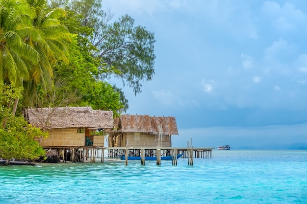 Indonesia. Una isla tropical cubierta de selva. Tarde nublada. Chozas sobre pilotes en el agua. Yate en la distancia