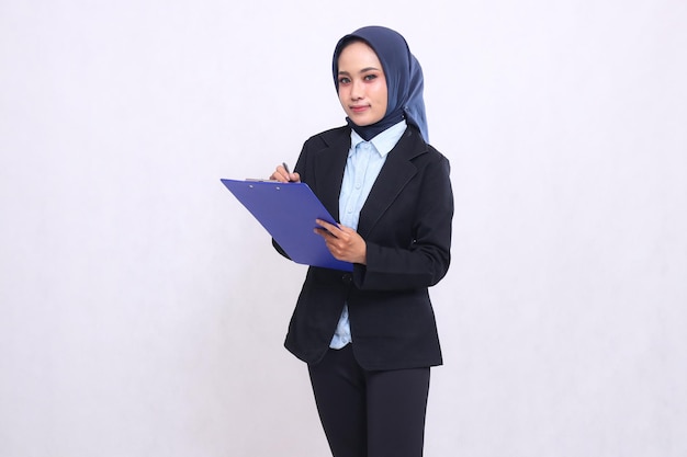 Indonesia mujer de oficina madura con hijab de pie mirando a la cámara escribiendo escritorio de trabajo en el portapapeles