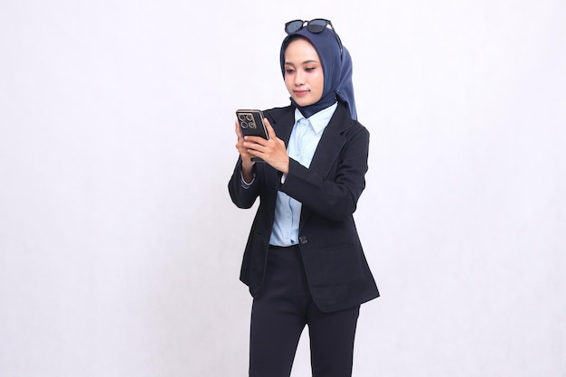 Indonesien reife Bürofrau mit Hijab steht lächelnd und trägt ein Smartphone-Gadget für Online-S