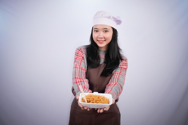 Indonesische asiatische Frau in Chefuniform zeigt gebratene Nudeln in einem Behälter