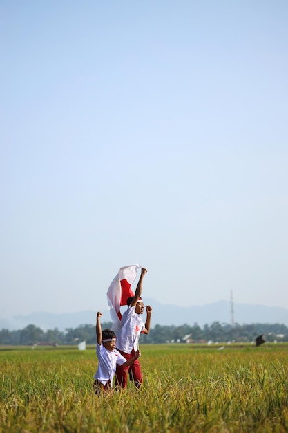 Indonesische Schüler, die Uniform tragen, heben ihre Hände, während sie die rot-weiße Flagge in t halten