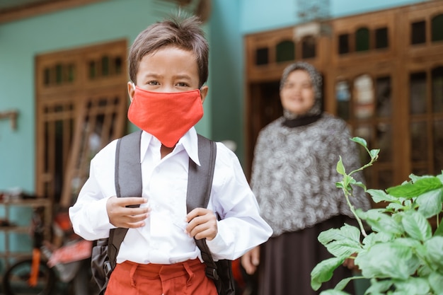 Indonesischer asiatischer Grundschüler, der eine Maske trägt, bevor er zur Schule geht