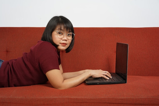 Indonesisches Mädchen oder Frau mit Laptop für die Arbeit oder Online-Klasse auf der Couch asiatische Frau