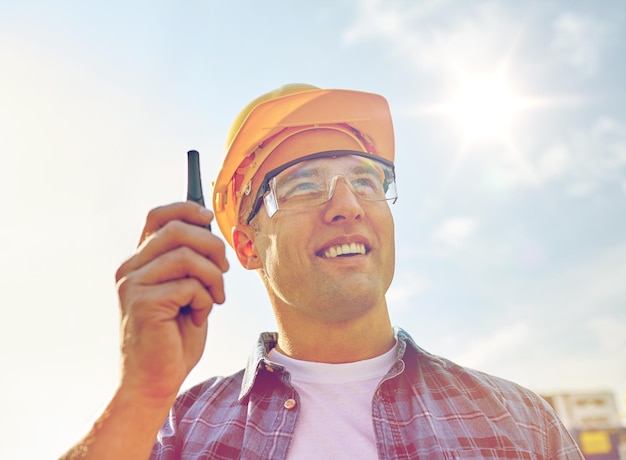 Foto industria, construcción, tecnología y concepto de personas - cierre de constructor masculino en casco con walkie talkie o radio al aire libre