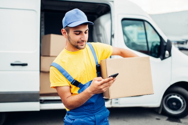 Industria de distribución de carga, servicio de entrega. Trabajador en uniforme con caja y teléfono móvil en manos. Contenedor vacío