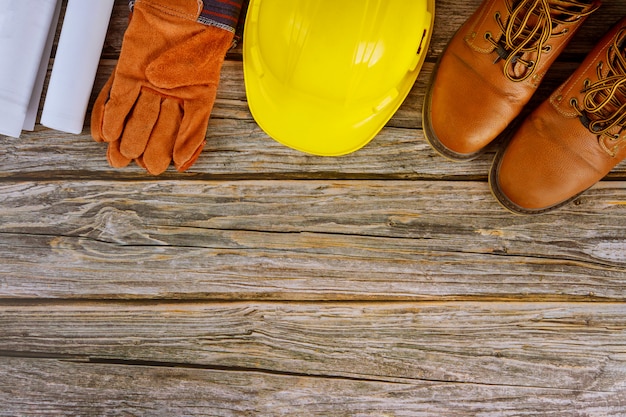 Industriearbeiterarchitekt mit Blaupausen in der Büroansicht stellte Schutzarbeitskleidung-Arbeitsstiefel auf gelbem Schutzhelm ein