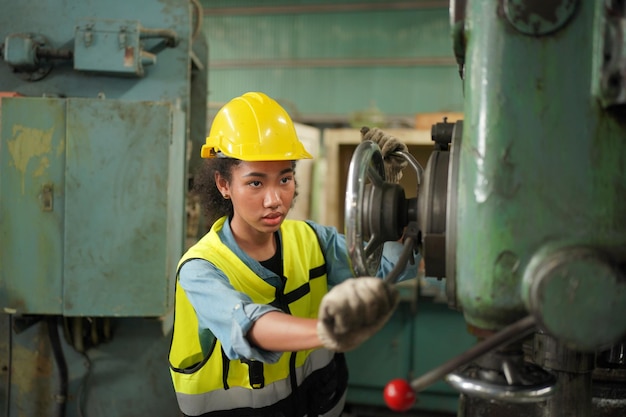 Industriearbeiterin im Schutzhelm mit Schwerindustrie-Fertigungsfabrik im Hintergrund mit verschiedenen Metallarbeiten-Projektteilen. Arbeit in der Schwerindustrie-Fertigungsfabrik.