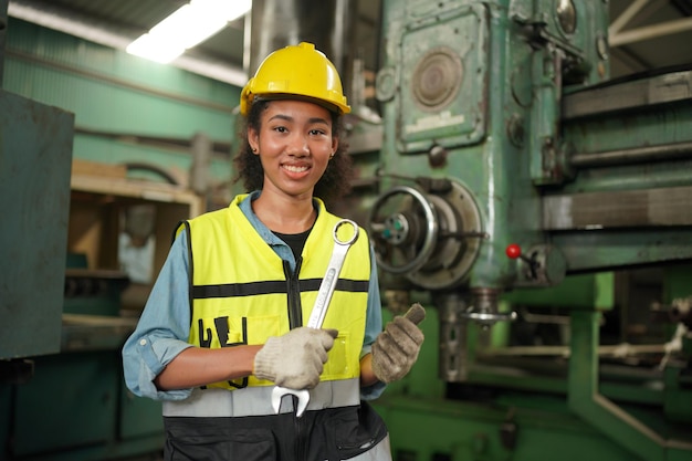 Industriearbeiterin im Schutzhelm mit Schwerindustrie-Fertigungsfabrik im Hintergrund mit verschiedenen Metallarbeiten-Projektteilen. Arbeit in der Schwerindustrie-Fertigungsfabrik.