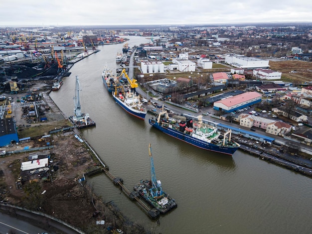 Industriekräne, die Frachtcontainer gegen den grauen Himmel in der Nähe des Meeres im Hafen heben. Draufsicht, Luftaufnahme