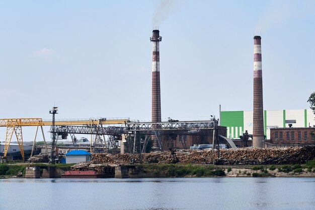 Industrielandschaft, Zellstoff- und Papierfabrik mit Holzstapeln und Schornsteinen am Fluss