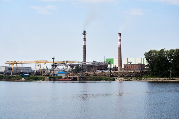 Industrielandschaft, Zellstoff- und Papierfabrik mit Holzstapeln und Schornsteinen am Fluss