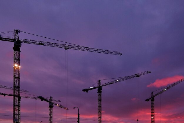 Industrieller Hintergrund mit Baukränenschattenbildern über erstaunlichem Sonnenunterganghimmel