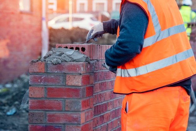 Industrieller Maurer, der auf der Baustelle Ziegel auf Zementmischung legt