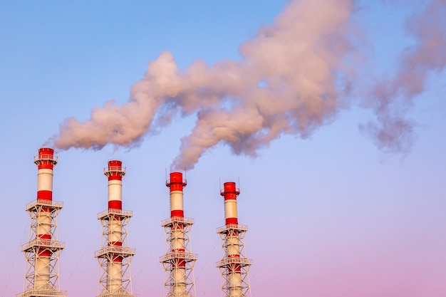 Industrielles Konzept. Rauchende Schornsteine oder Fabrikpfeifen gegen den blauen Dämmerungshimmel.