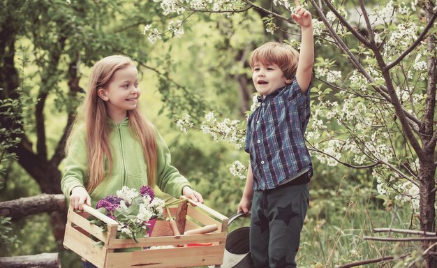La infancia y el crecimiento de los niños juegan en el jardín de primavera, un niño lindo levanta la mano y la niña mira
