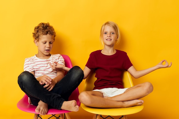 Infância de duas crianças alegres sentadas em cadeiras juntas em fundo colorido