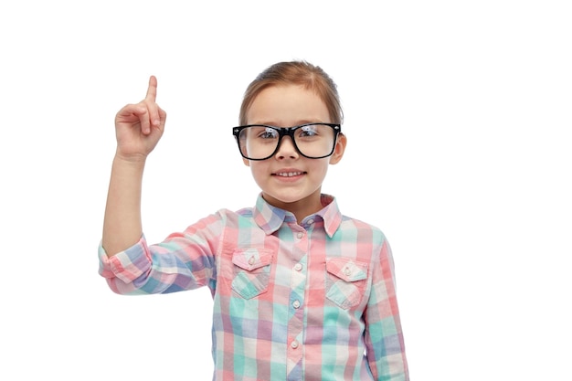 la infancia, la escuela, la educación, la visión y el concepto de la gente - niña feliz con anteojos apuntando con el dedo hacia arriba