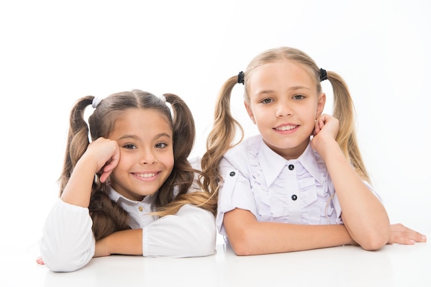 Infância feliz Alunas sentam-se à mesa fundo branco Alunas amigas emocionais Alunas adoráveis De volta à escola Conceito de educação Garotas bonitas melhores amigas Estilo formal