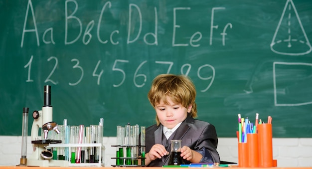 Infância feliz Criança gosta de estudar Menino perto de microscópio e tubos de ensaio na sala de aula da escola Conceito de conhecimento Dia do conhecimento Conhecimento básico educação primária Criança estuda biologia química