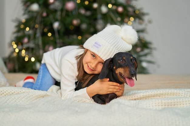 Infancia feliz, cuento de hadas mágico de Navidad. Una niña se ríe con su amigo, un perro salchicha, cerca del árbol de Navidad.