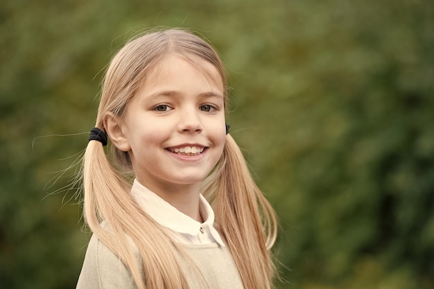 Infância feliz e puericultura Criança com sorriso no rosto bonito ao ar livre Menina com longos cabelos loiros Criança de beleza com aparência e pele fresca Olhar de beleza e espaço de cópia de cuidados com a pele