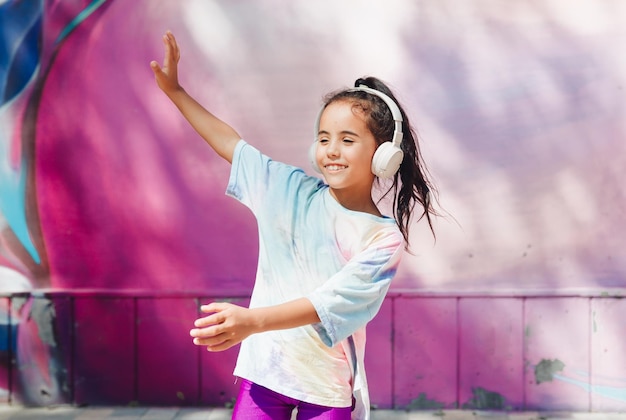 Infancia feliz Una niña feliz escucha música y baila en la calle Un niño pequeño con auriculares primavera y otoño moda música favorita en auriculares generación z