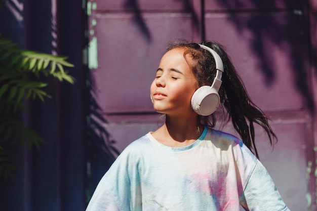 Infancia feliz Una niña feliz escucha música y baila en la calle Un niño pequeño con auriculares primavera y otoño moda música favorita en auriculares generación z