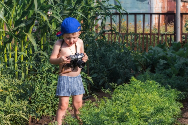 Infancia feliz. El pequeño bebé sostiene una cámara e intenta tomar la foto en el jardín. Pequeño fotógrafo.