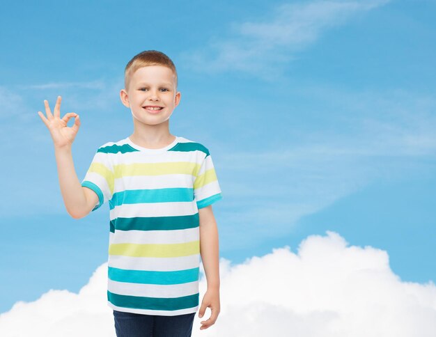 infancia, gesto y concepto de la gente - niño pequeño sonriente con ropa informal haciendo un buen gesto sobre el fondo del cielo azul