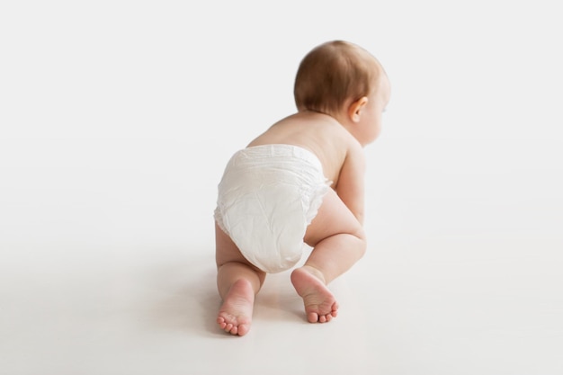 Foto infancia, infancia y concepto de la gente - niño pequeño o niña en pañales arrastrándose en el suelo blanco