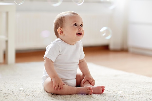 infância, infância e conceito de pessoas - bebezinho feliz ou menina sentada no chão com bolhas de sabão em casa