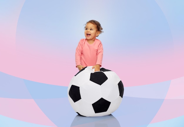 Foto infância, jogo, esporte, futebol e conceito de pessoas - feliz garotinha afro-americana brincando com bola sobre fundo rosa violeta