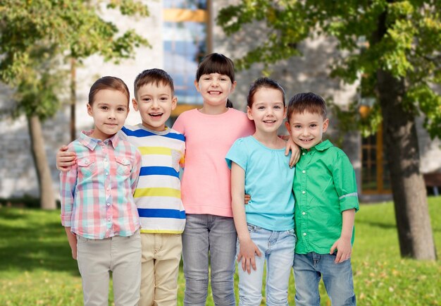 Foto la infancia, la moda, la amistad y el concepto de la gente - grupo de niños pequeños felices y sonrientes abrazándose sobre el fondo del campus de verano