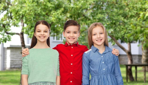 la infancia, la moda, la amistad y el concepto de la gente - niños y niñas sonrientes felices abrazándose sobre el fondo del patio trasero de la casa privada