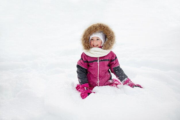 infancia, moda, temporada y concepto de la gente - cara de niño o niña feliz con ropa de invierno en la nieve