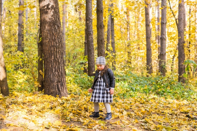 Infancia, otoño, concepto de personas - niña caminando en hojas de otoño.