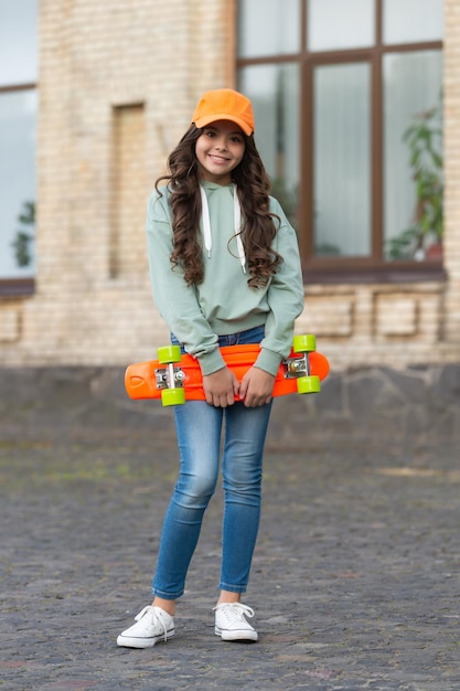 Foto infancia de una patinadora adolescente alegre fuera de la infancia de una patinadora adolescente en la calle