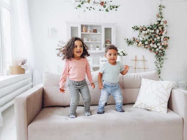 Infancia sin preocupaciones Niños afroamericanos felices saltando en el sofá jugando juntos en casa hermano y hermana divirtiéndose en la sala de estar