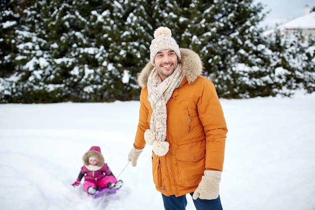 infancia, trineo, ocio, temporada y concepto de la gente - hombre o padre feliz que lleva a un niño pequeño en trineo en invierno