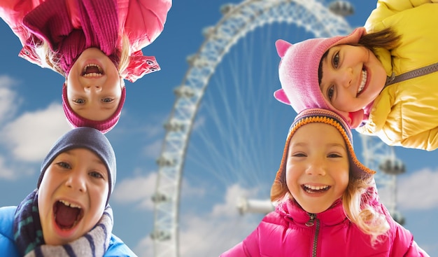 la infancia, el turismo, los viajes, las vacaciones y el concepto de la gente - los niños pequeños felices se enfrentan al aire libre sobre el fondo de la rueda del ferry de Londres