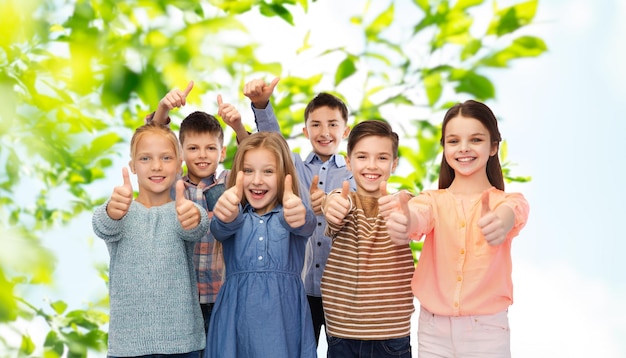 infancia, verano, gesto y concepto de la gente - niños sonrientes felices mostrando los pulgares hacia arriba sobre el fondo natural verde