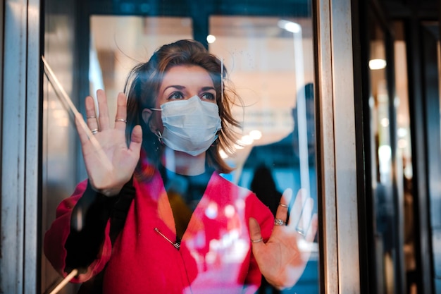 Infektion stoppen. frau zeigt stop-geste durch glastür, es gibt keinen ausgang. mädchen trägt an einem öffentlichen ort eine schutzmaske gegen infektionskrankheiten grippe. das konzept der gesundheit, die quarantäne.